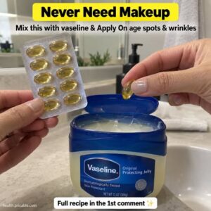 A close-up shot of a small jar of Vaseline a Vitamin E capsule and a small mixing bowl with a spoon arranged on a rustic