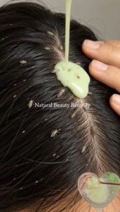 A person s hand gently applying a natural oil mixture to the hair and scalp of another person focusing on the roots The 