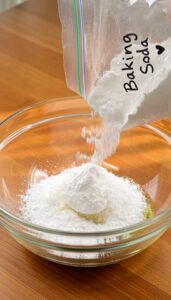 A close-up shot of small bowls containing baking soda Vaseline and baby oil arranged neatly on a wooden surface with sof