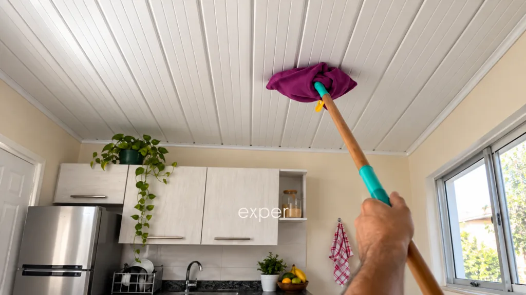 A person s arm using a long-handled duster to clean a white paneled ceiling in a kitchen setting