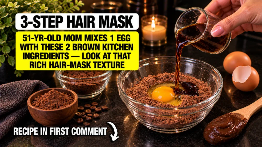 A hand mixing dark liquid into a clear glass bowl containing a bright yellow egg yolk and brown cocoa powder for a DIY h