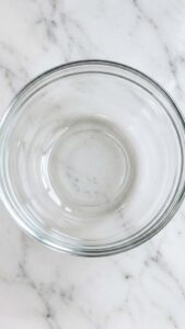 A close-up shot of a small glass bowl containing a yellowish creamy mixture Next to it are a cut lemon a jar of honey an