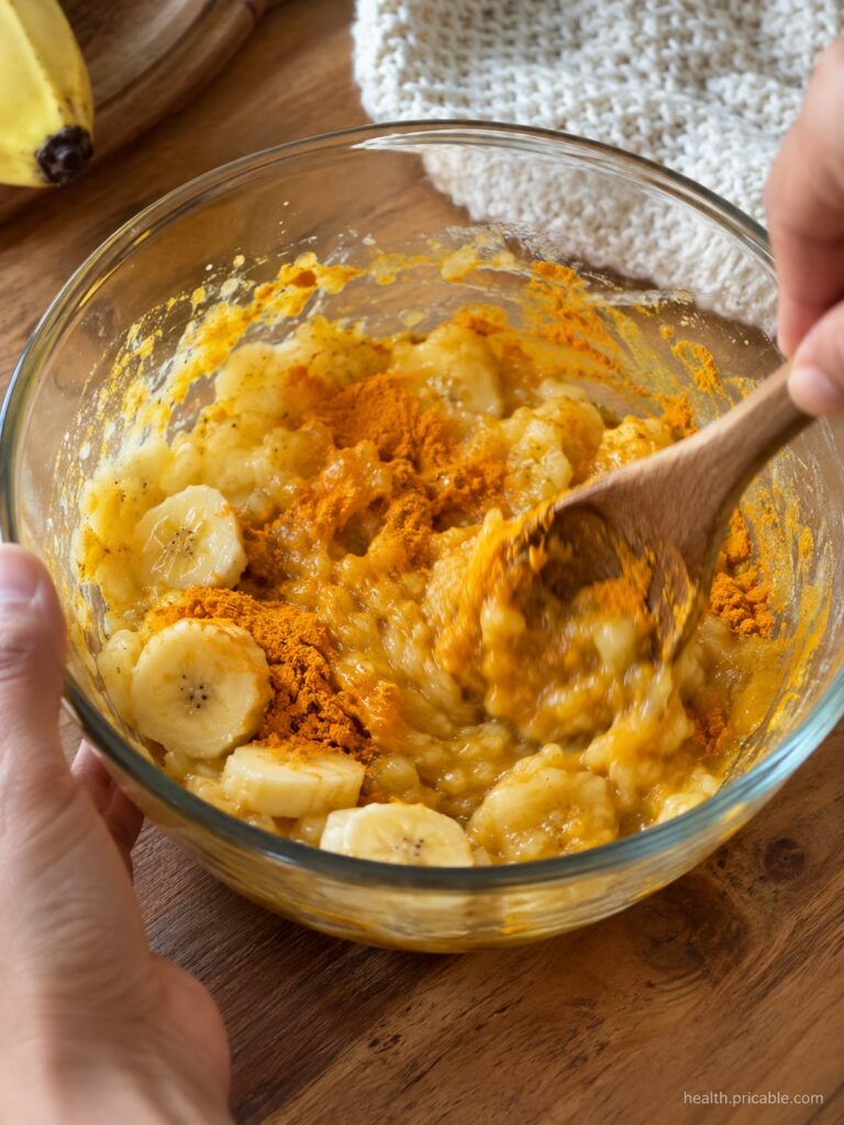 A small bowl with the three main ingredients half a ripe banana a small spoon with turmeric powder and a small dollop of