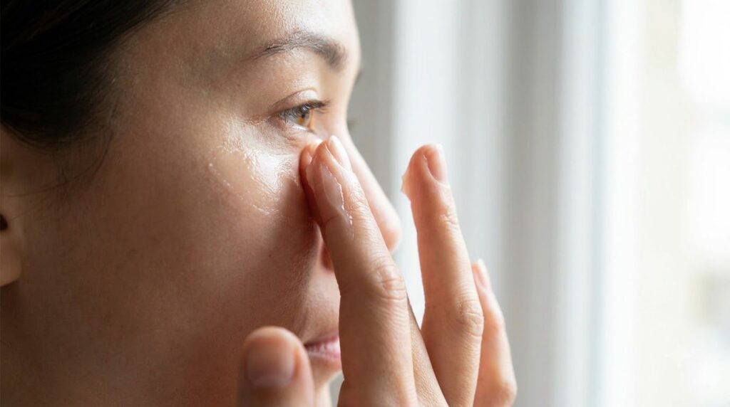 Close-up of a person s fingers gently massaging a small amount of warmed Vaseline onto the skin around their eye area hi