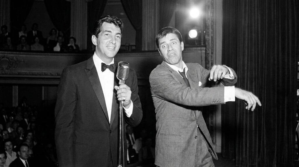 Black and white photo of Dean Martin and Jerry Lewis performing on stage with Martin looking suave and Lewis doing a com
