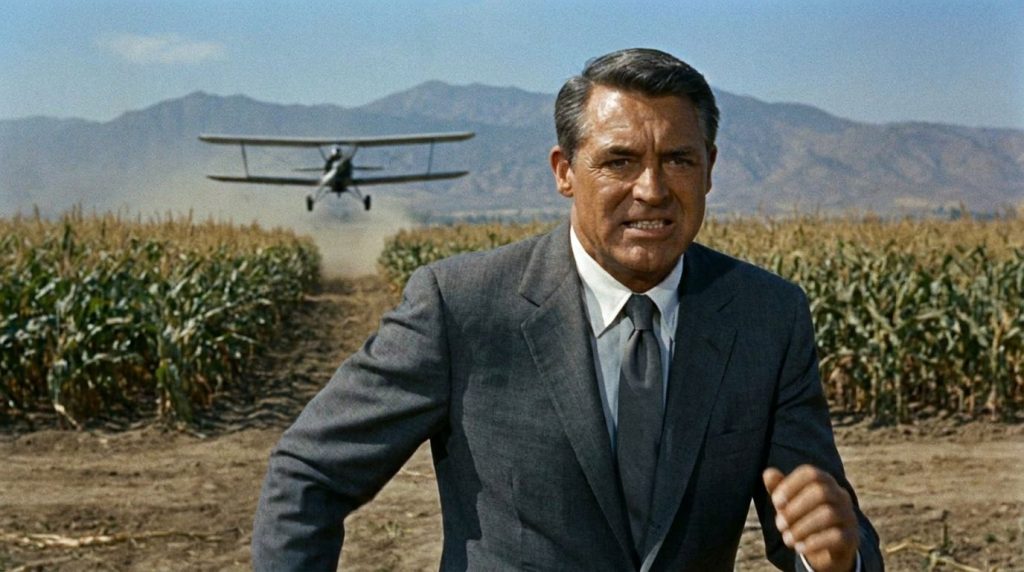 Cary Grant in a sophisticated suit looking suave and confident in a scene from North by Northwest possibly running or lo