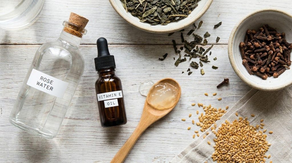 Various natural ingredients for DIY skincare laid out neatly whole cloves flaxseeds a bottle of rose water green tea lea
