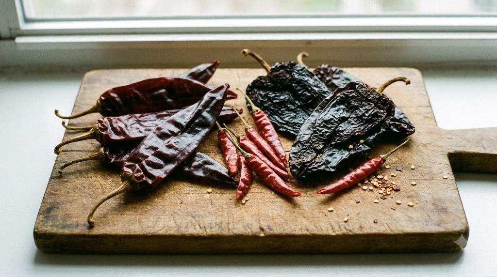 A selection of dried chiles guajillo ancho arbol laid out on a wooden cutting board