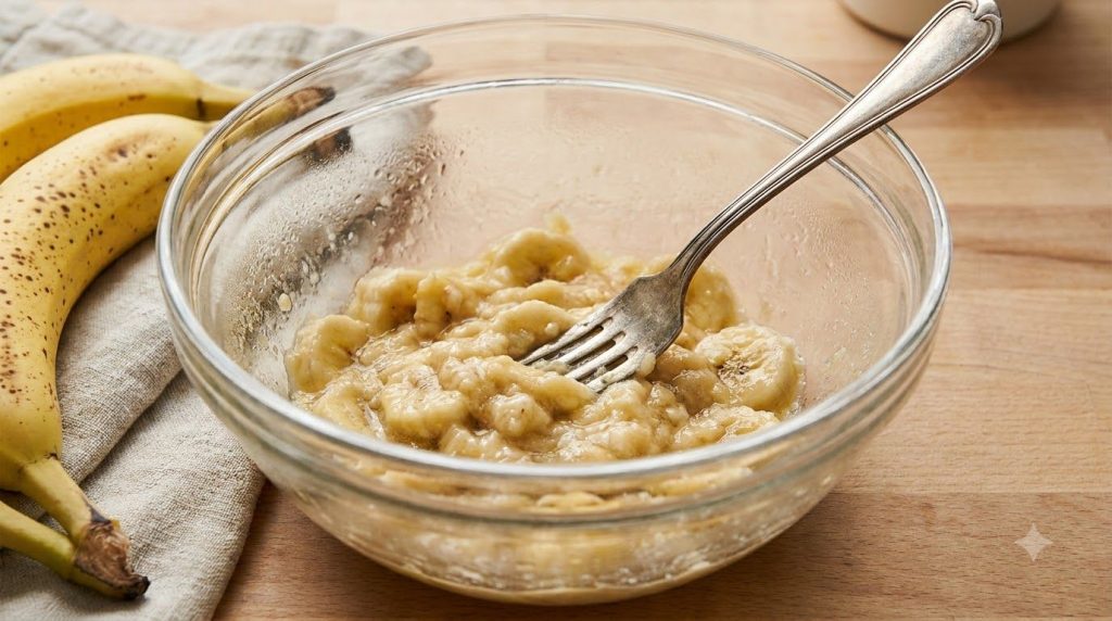 A close-up of mashed ripe bananas in a mixing bowl with a fork