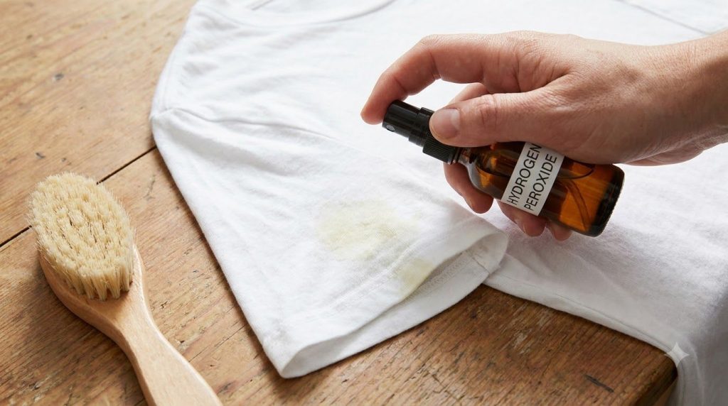 A close-up of a white stained garment being spot-treated with hydrogen peroxide and a small brush