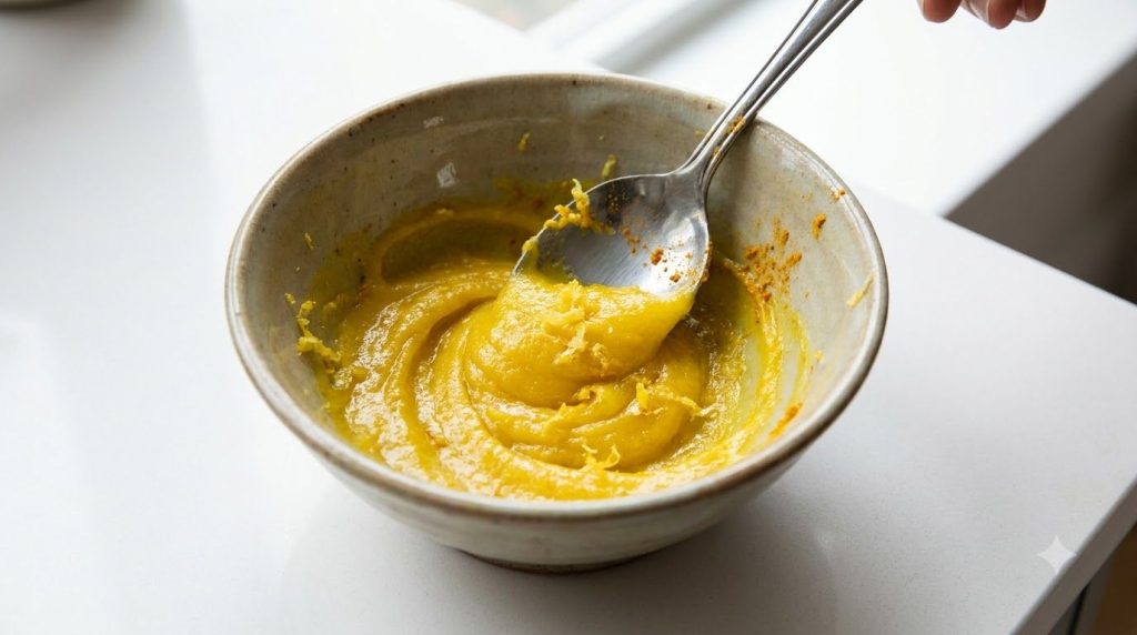 A close-up of the Vaseline lemon and turmeric mixture being stirred into a smooth yellow paste in a small bowl