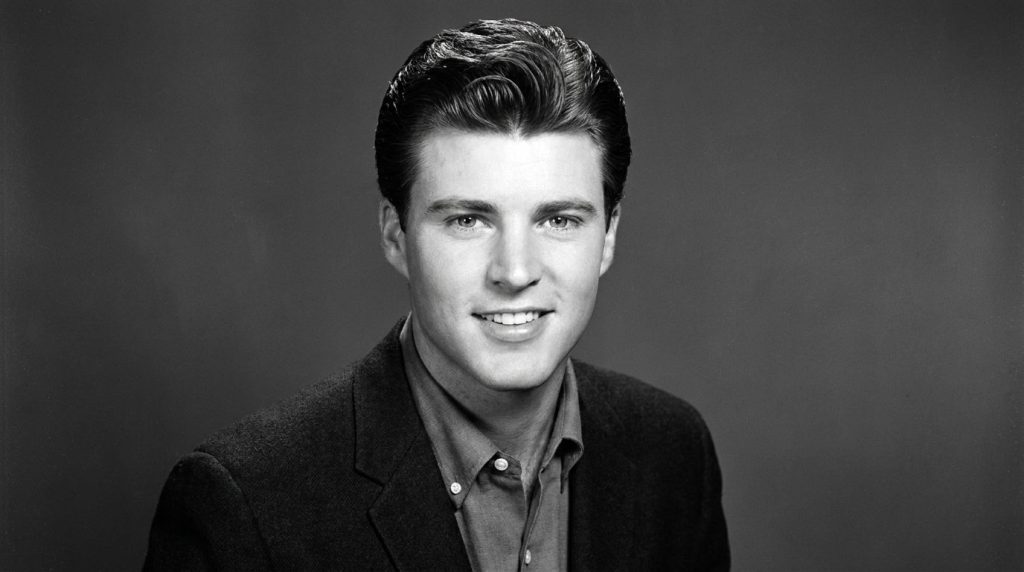 A vintage portrait of Rick Nelson in his younger years perhaps from the late 1950s or early 1960s smiling confidently wi