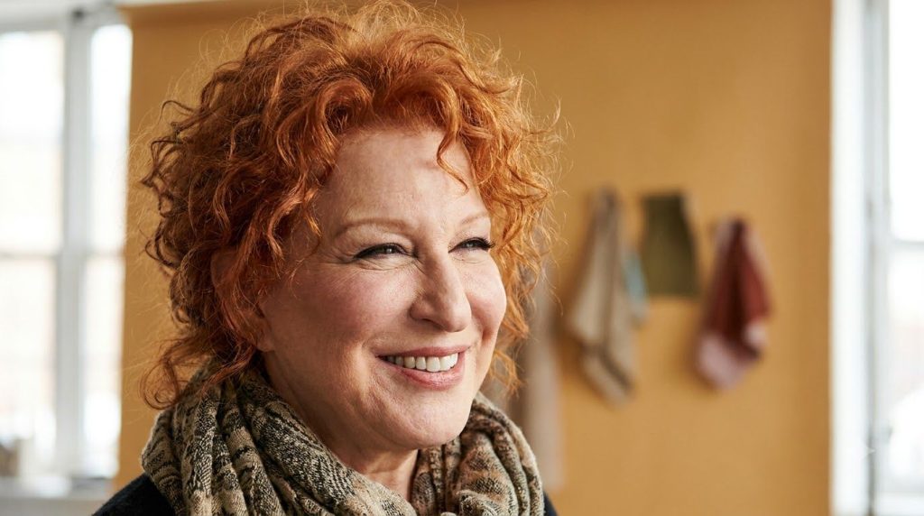 A vibrant portrait of Bette Midler smiling showcasing her distinctive red curly hair and charismatic expression
