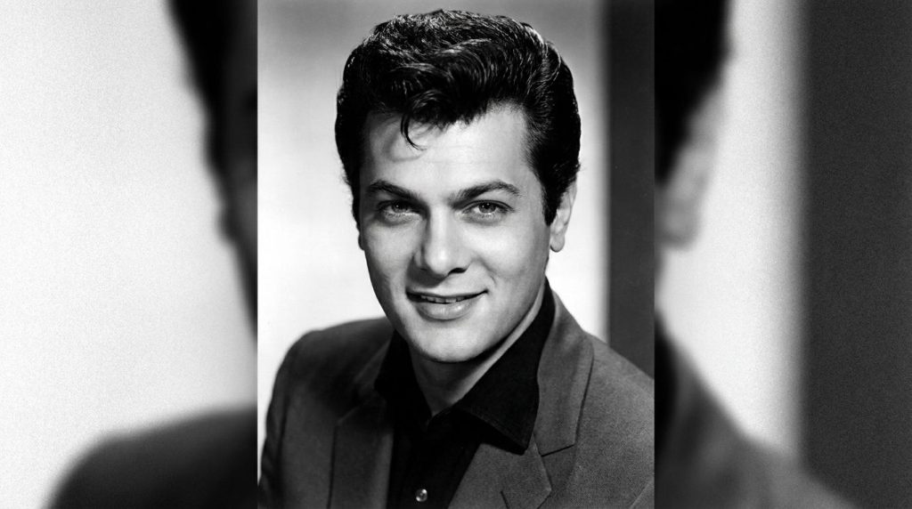 A classic black and white publicity photo of a young Tony Curtis from the 1950s showing his signature hairstyle and conf