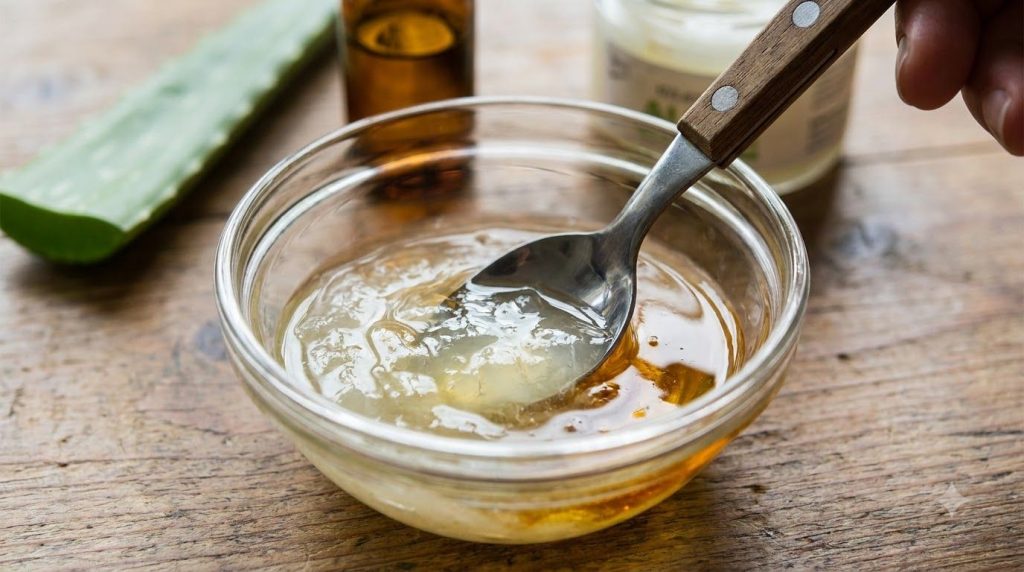 Close-up of a small glass bowl containing the mixed ingredients aloe vera gel almond oil and vitamin E oil with a spoon 