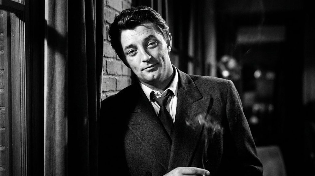A black and white portrait of Robert Mitchum looking cool and slightly cynical wearing a suit and tie embodying his clas