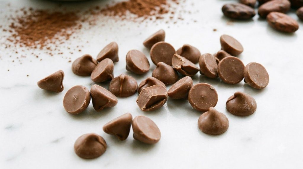 A close-up shot of homemade milk chocolate chips light brown in color scattered on a white surface