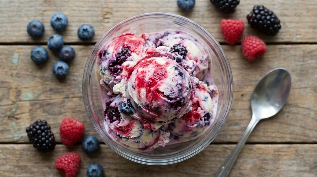 Colorful scoops of mixed berry ice cream showcasing swirls of red purple and blue Fresh berries scattered around