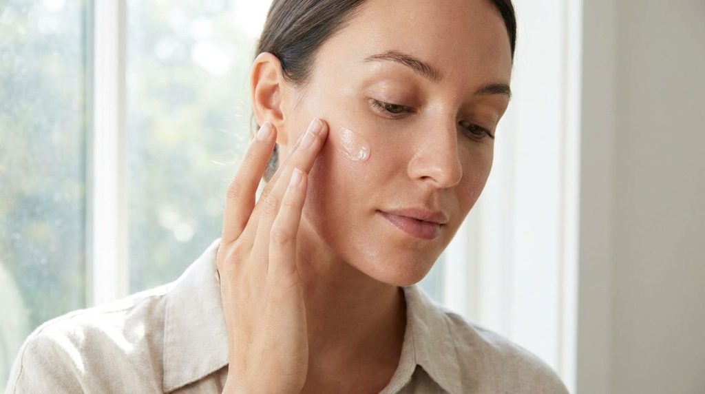 A woman gently applying a homemade balm to her cheek with her fingertips