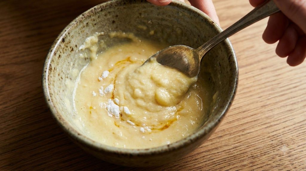 A close-up shot of a small bowl where Vaseline baking soda and egg yolk are being mixed into a creamy yellow paste with 