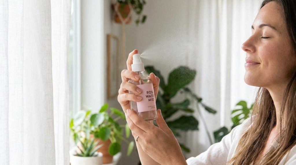 A woman s hands spritzing rose water onto her face after rinsing off a mask looking refreshed