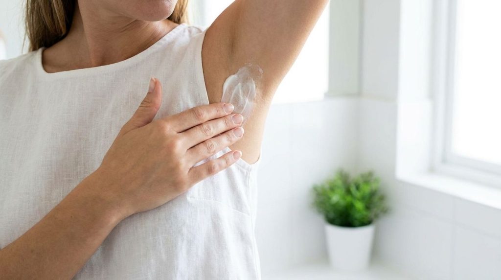 A woman gently applying a white creamy mask to her clean underarm area with her fingertips focusing on the careful appli