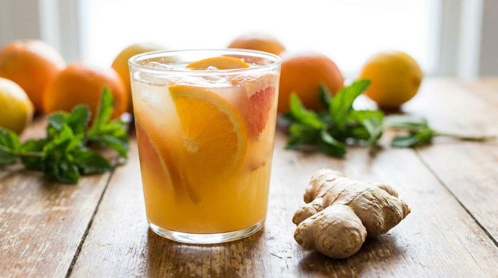 A bright orange and yellow citrus drink in a glass with orange and grapefruit slices A small piece of ginger is visible