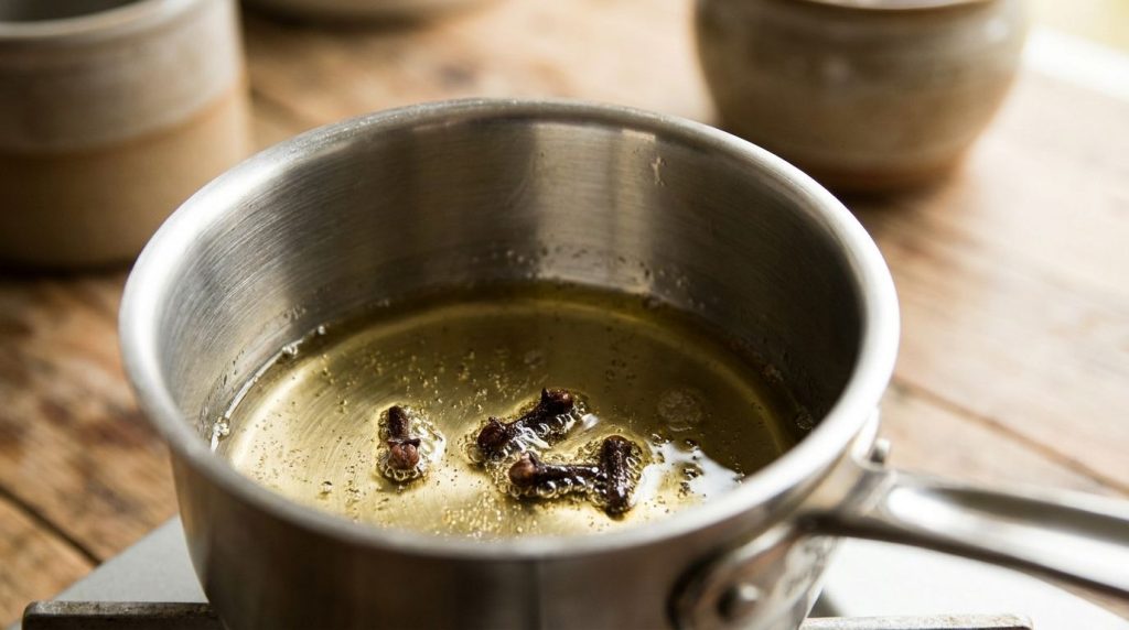 A close-up of dried whole cloves simmering gently in a small saucepan with a clear oil illustrating the infusion process