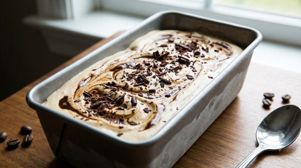 A close-up of no-churn coffee ice cream in a loaf pan showing swirls of coffee and cream ready to be scooped It looks de