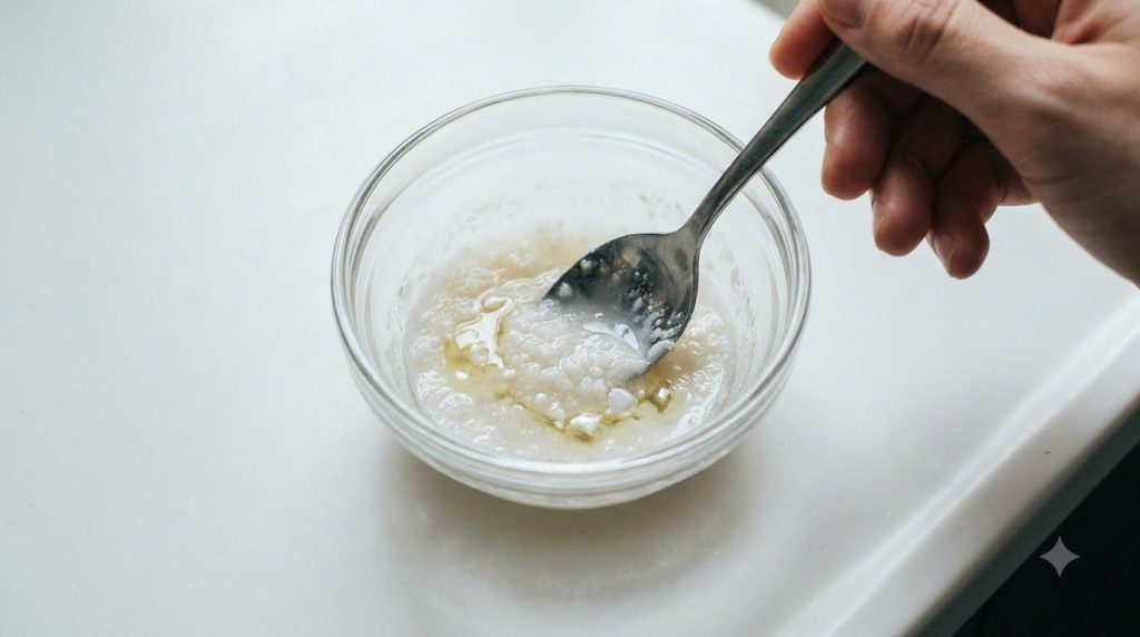 Close-up of a small bowl with crushed aspirin and baby oil being mixed into a paste with a spoon