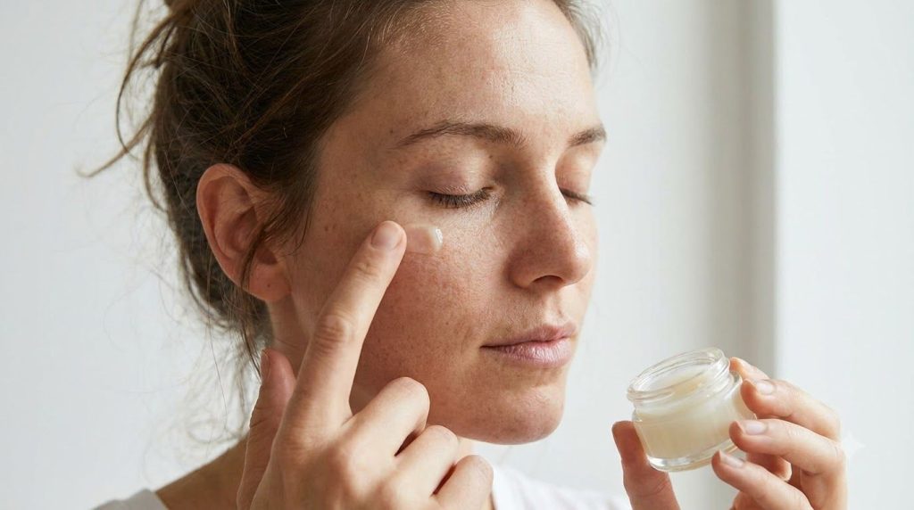 A woman gently applying the homemade Vaseline balm to the skin under her eyes with her fingertip showing a close-up of h