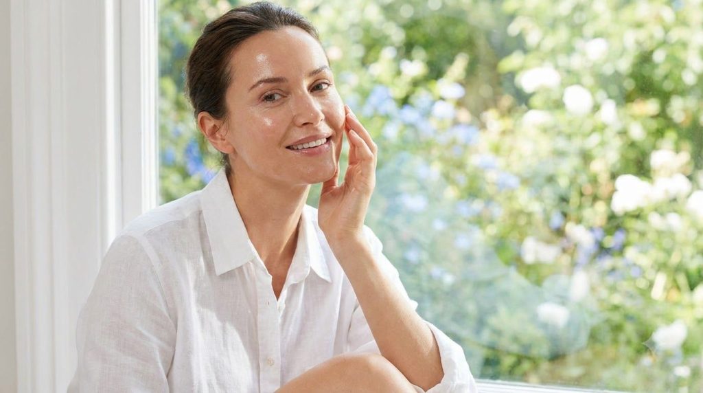 A woman smiling with clear radiant skin after using a face pack touching her cheek gently