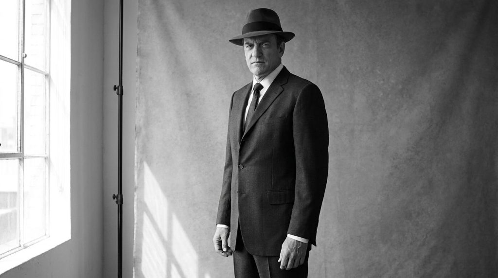 Black and white publicity photo of James Arness in a suit showcasing his tall stature