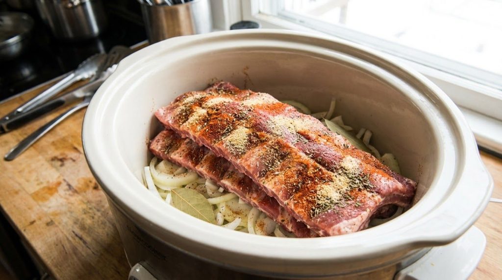 Pork ribs seasoned and placed in a slow cooker over sliced onions ready for the sauce