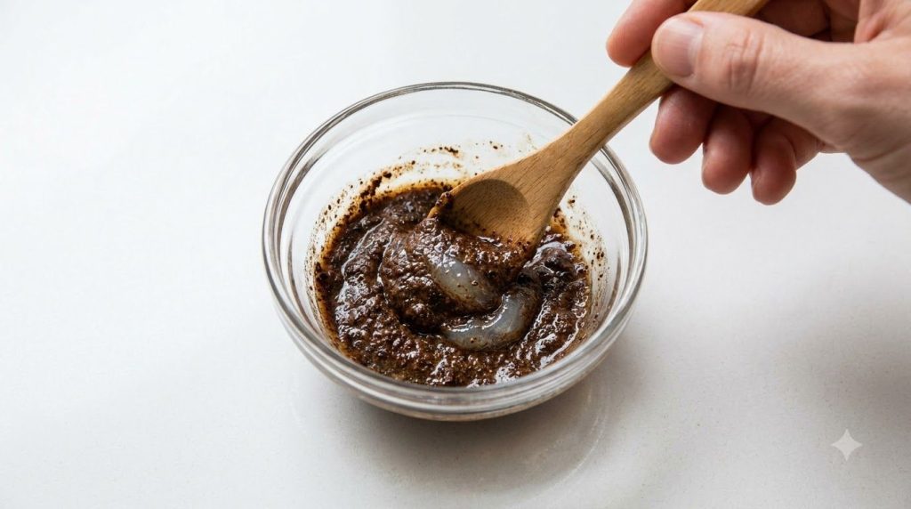 A close-up of a small bowl containing a mixture of coffee grounds and Vaseline being stirred with a small wooden spoon T