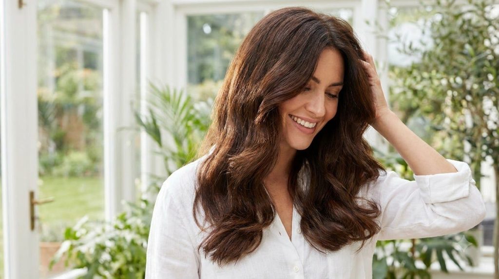 A woman gently running her fingers through her noticeably thicker shinier hair She has a natural happy expression convey