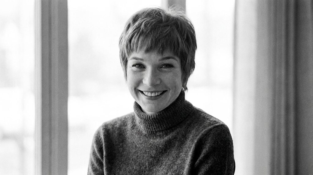 A black and white publicity photo of Shirley MacLaine from the 1960s smiling brightly with her characteristic short hair