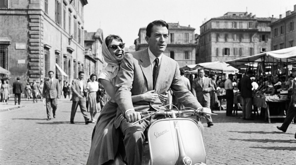 Audrey Hepburn riding a scooter with Gregory Peck in a scene from Roman Holiday black and white