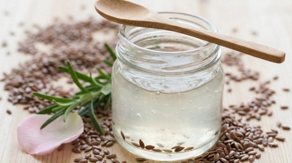 A close-up of a glass jar filled with a translucent slightly viscous flaxseed gel with some whole flaxseeds visible at t