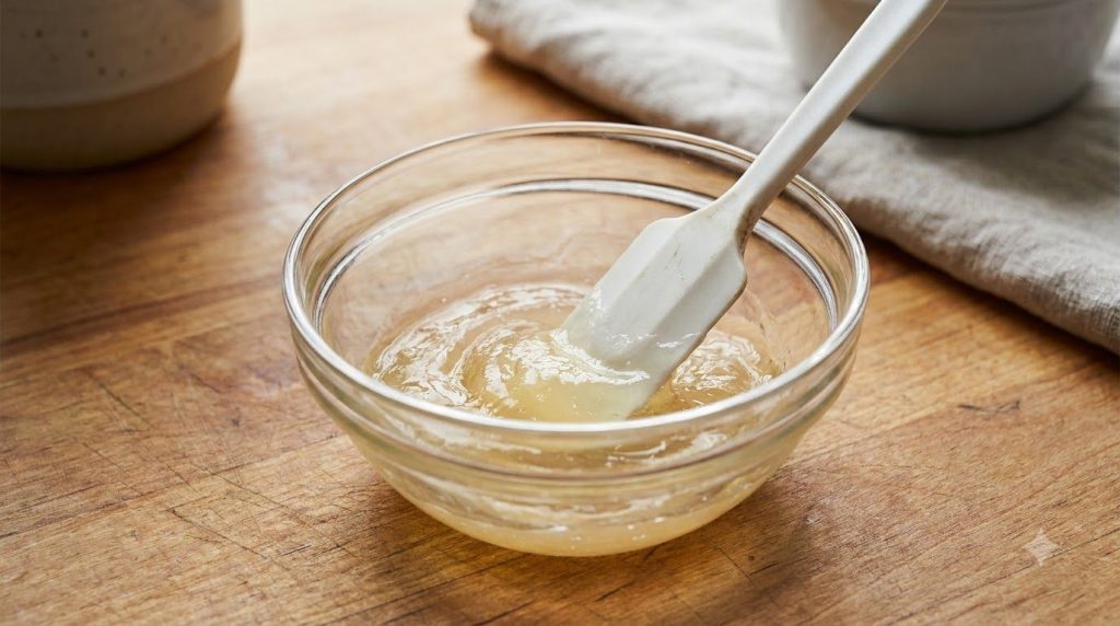 Close-up of a small glass bowl where baby oil aloe vera gel vitamin C powder and turmeric powder are being mixed with a 