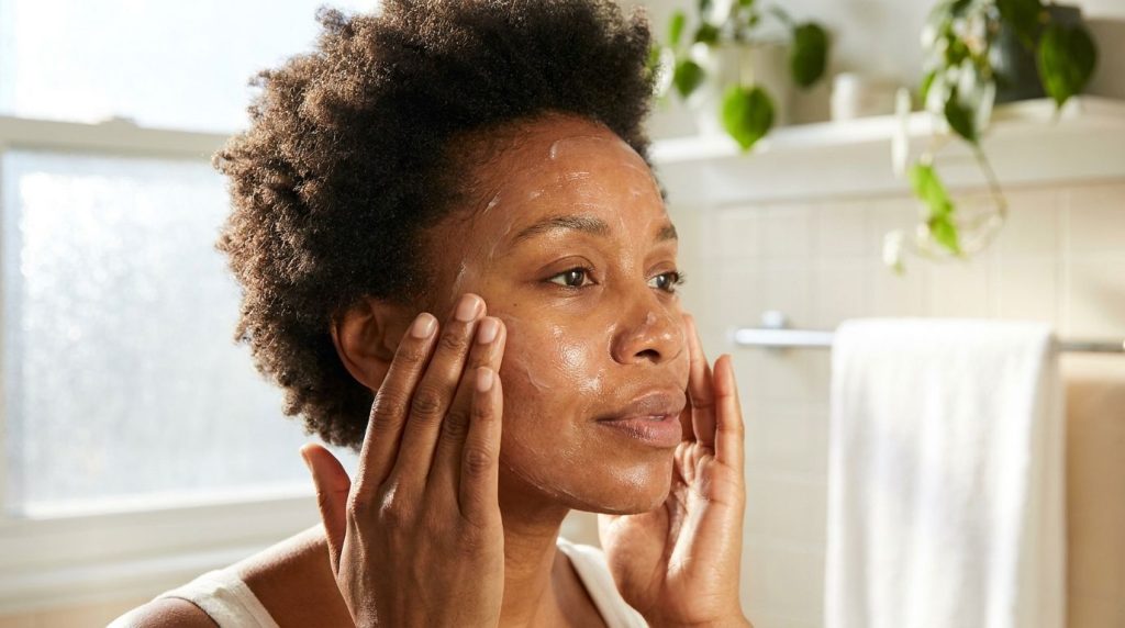 A close-up of a woman applying the Vaseline honey and aloe vera mask to her face with her fingertips