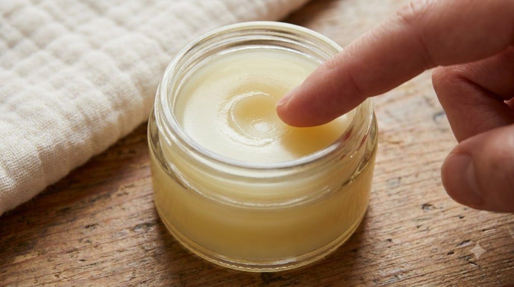 A close-up shot of a small clean glass jar filled with the freshly mixed baby oil and petroleum jelly balm showing its s