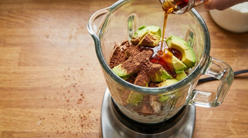 Close-up of ripe avocado chunks being added to a blender with other ingredients