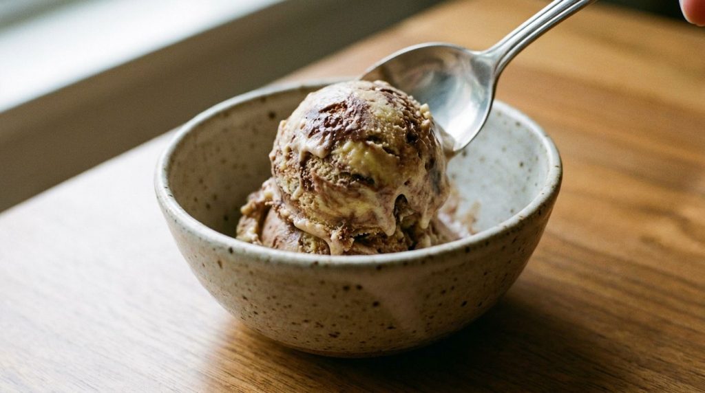 A close-up shot of a scoop of homemade banana chocolate fudge ice cream being placed into a serving bowl
