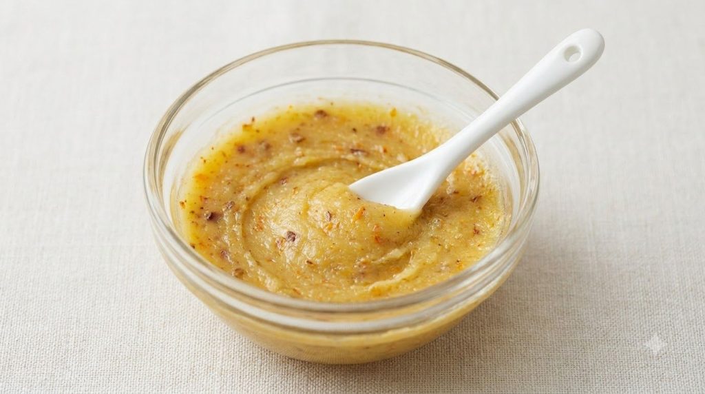 A close-up of a small bowl containing the mixed Vaseline balm with orange peel powder and ground cloves being stirred wi