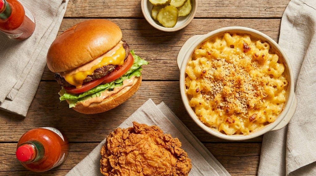 A flat lay of a classic cheeseburger a bowl of macaroni and cheese and a piece of fried chicken