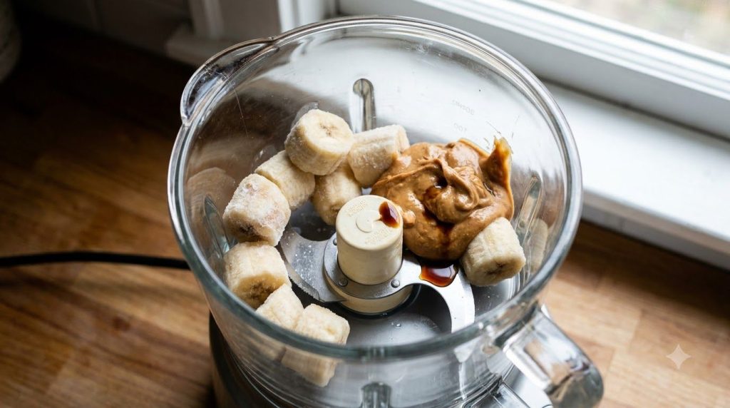 Frozen banana slices peanut butter and vanilla extract inside a food processor bowl