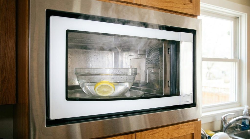 A glass bowl filled with a clear liquid vinegar and water and a lemon slice inside a microwave generating steam