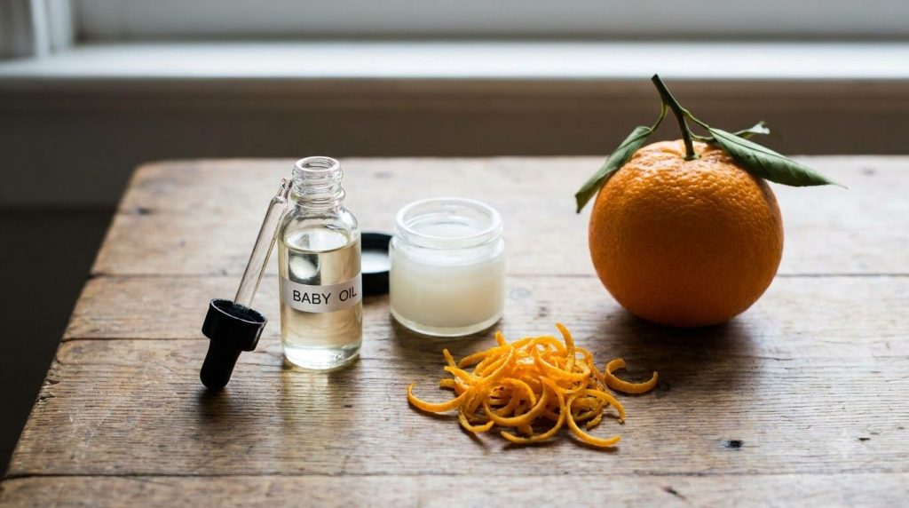 Ingredients for Smoothing Brightening Oil baby oil petroleum jelly and orange zest or orange essential oil on a clean co