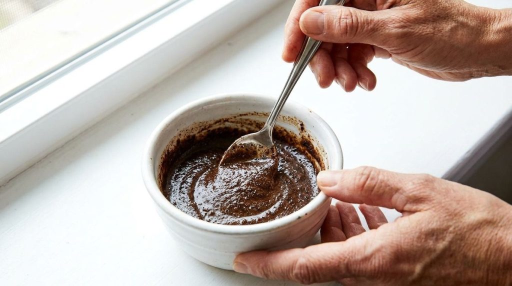 Close-up of hands mixing Vaseline baby oil and finely ground coffee in a small bowl with a spoon The texture is a creamy